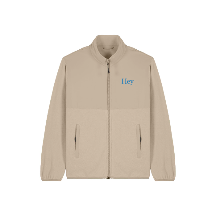 Stanley/Stella's STJU242 Stanley/Stella Trekker is a beige zip-up fleece jacket crafted from recycled polyester, featuring "Hey" embroidered in blue on the chest. It includes elastic cuffs and two front pockets, making it the perfect unisex jacket for versatile styling.