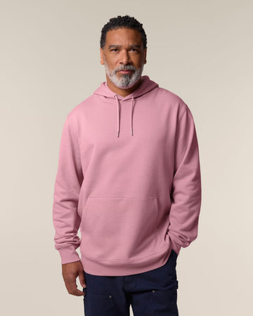 A man is in a pink Stanley/Stella STSU177 Stella/Stella Cruiser 2.0 The Iconic Unisex Hoodie Sweatshirt with hands relaxed in the kangaroo pocket against a neutral background.