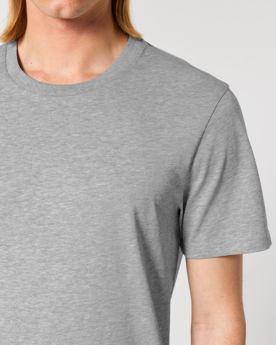 Close-up of a person wearing the Stanley/Stella Crafter The Iconic Mid-Light Unisex T-shirt in gray, made of organic cotton. The top half of their body is visible, and their hair is partially shown. The background is neutral.