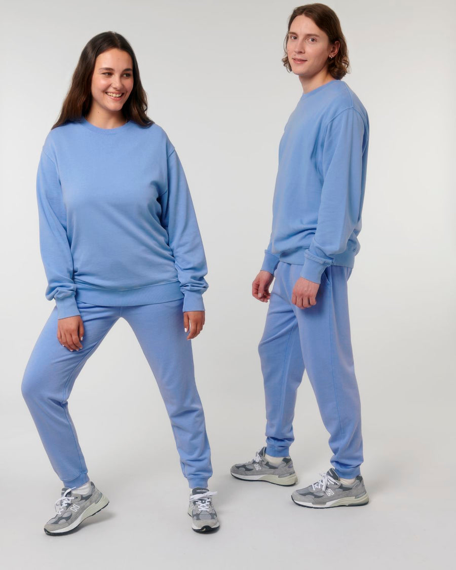 Two people wearing garment-dyed light blue MyNeedsAreSimple STSU085 Stanley Stella Matcher Vintage Unisex Medium Fit Crew Neck Sweatshirts pose against a plain white background. Both are standing, facing the camera, and smiling in their unisex sweatshirts made from organic cotton.