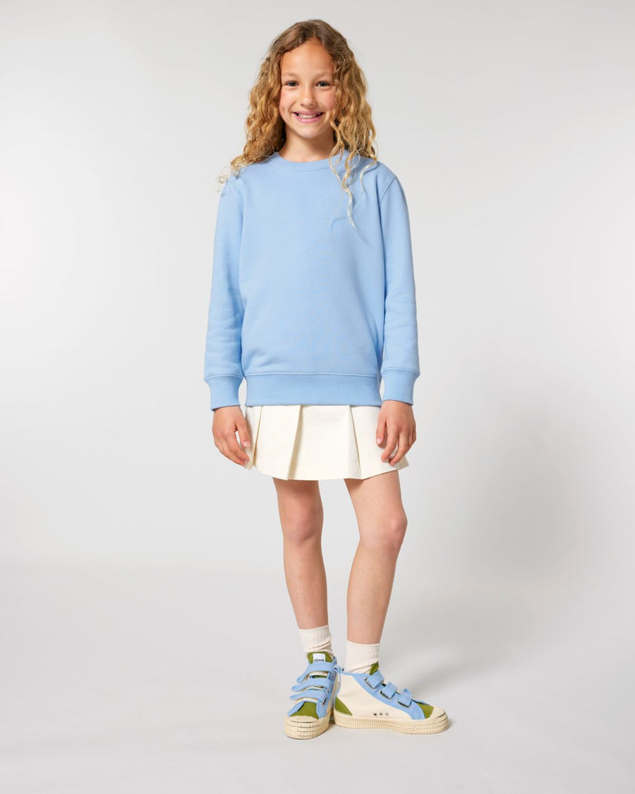 A girl wearing a Stanley/Stella organic cotton blue sweater and white skirt.