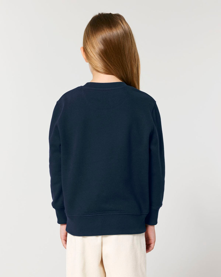 The back view of a girl wearing a STSK181 Stella/Stella Mini Changer 2.0 The Iconic Kids' Crew Neck Sweatshirt in navy by Stanley/Stella.