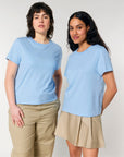Two women standing side by side, both wearing light blue STTW172 Stella Muser The Iconic Womens T-Shirts from Stanley/Stella made from organic cotton and beige bottoms. The woman on the left is in pants, while the woman on the right is in a skirt.