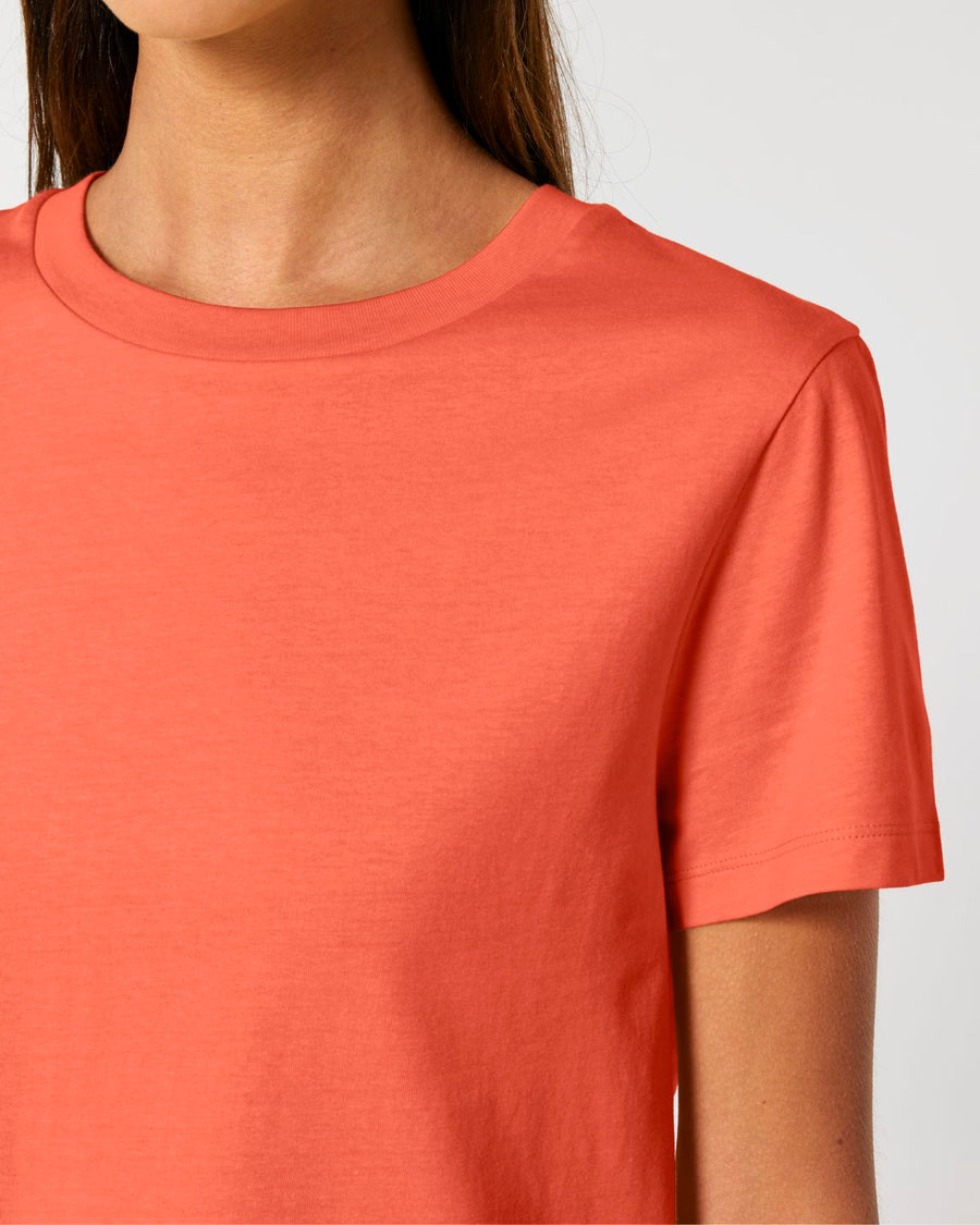 A person wearing a plain, short-sleeved, coral-colored STTW172 Stella Muser The Iconic Women's T-Shirt by Stanley/Stella made of organic cotton. The face is not visible.